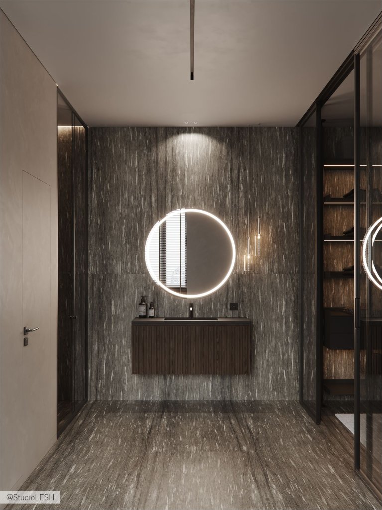 Интерьер современной ванной комнаты в темных тонах: круглое зеркало с подсветкой, душевая кабина со стеклянными дверями, подвесная тумба с раковиной.