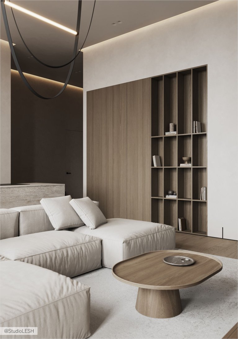 В гостиной с белыми стенами и деревянными панелями расположен угловой диван с подушками, круглый журнальный столик и встроенный книжный шкаф.