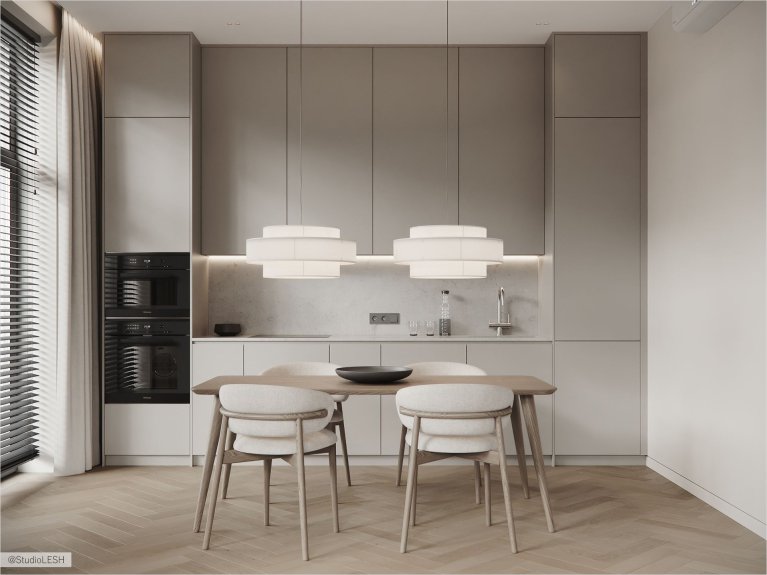 Интерьер кухни в светлых тонах с гладкими фасадами, встроенной техникой, двумя подвесными светильниками над обеденным столом и четырьмя стульями с мягкой обивкой