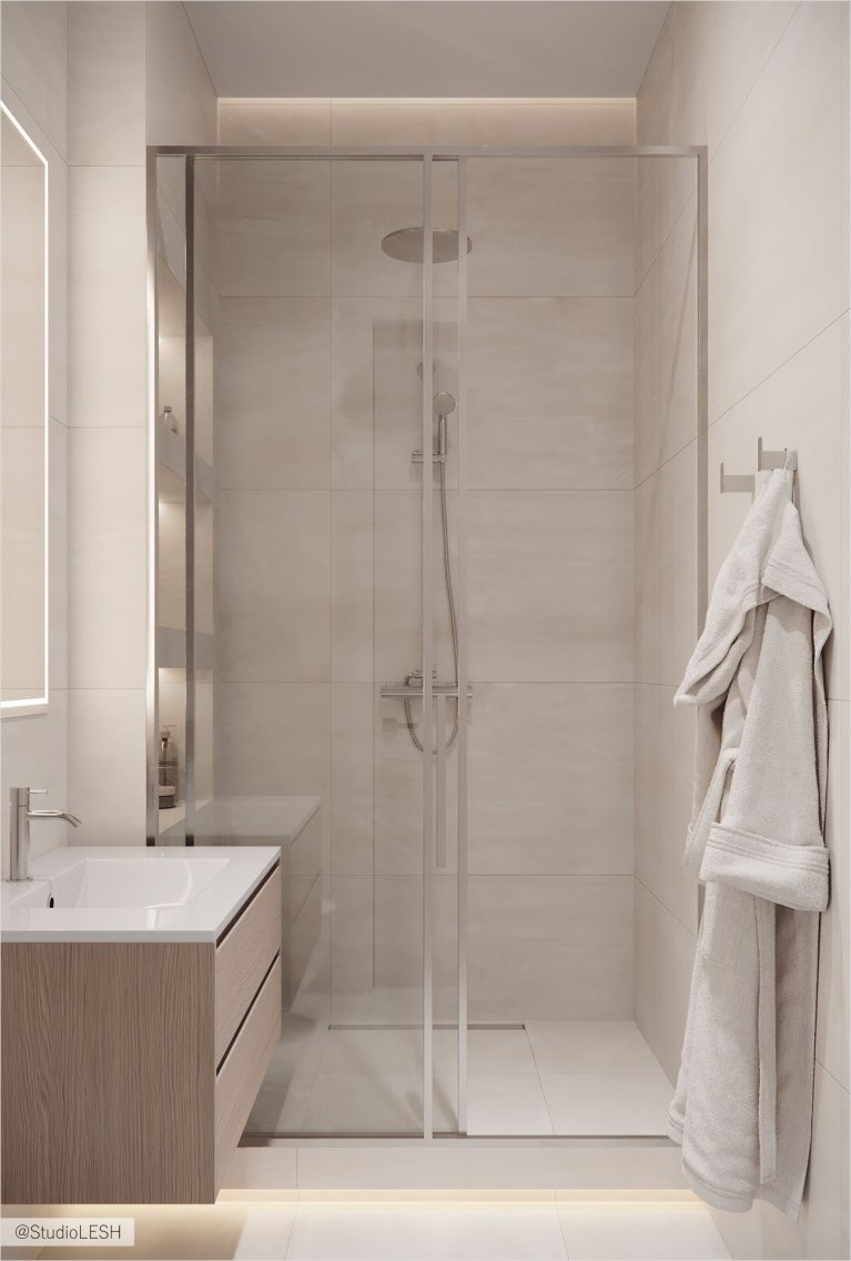 Стильная ванная комната с душевой кабиной с тропическим душем и стеклянной перегородкой. На переднем плане - подвесная тумба с раковиной и зеркалом с подсветкой. Справа висит мягкий белый халат