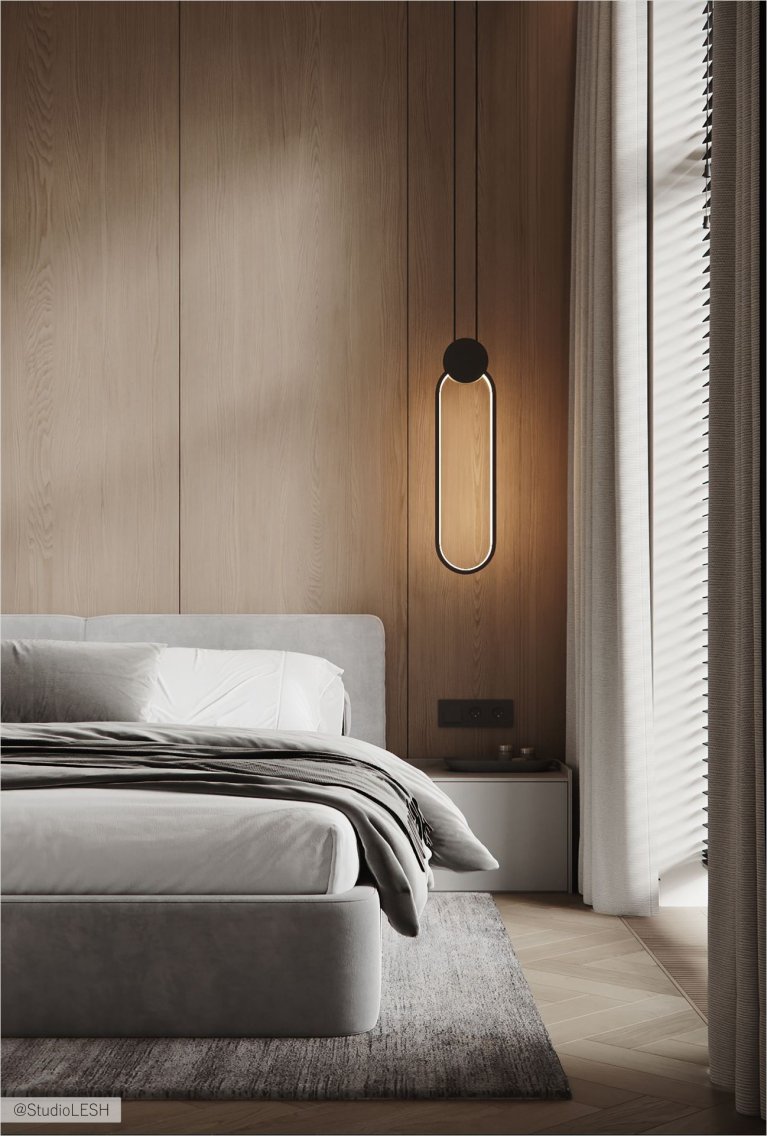 Уютная спальня с большой кроватью, застеленной серым покрывалом, и декоративными подушками. На стене за кроватью - деревянная панель, а по бокам - две тумбочки с лампами. В комнате также есть большое окно с жалюзи и плотными шторами, пропускающими мягкий свет