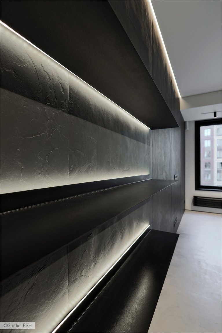 Стильная кухня с темными шкафами с гладкими фасадами, подчеркнутыми встроенной подсветкой. Подсветка создает игру света и тени, делая интерьер более выразительным. Минималистичный дизайн кухни подчеркивает ее современность и функциональность