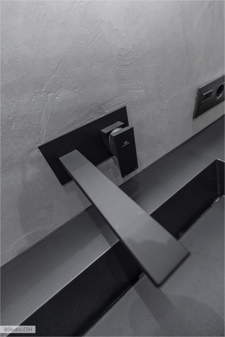 Стильная кухня с черным смесителем с гибким изливом, идеально подходящим для современной кухни. Смеситель установлен на темной столешнице рядом с темной раковиной. Видны также другие элементы кухонного гарнитура, выполненные в едином стиле, и рейлинг с крючками на заднем плане