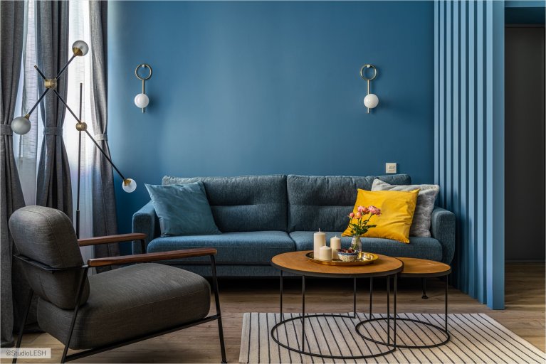Современная гостиная с синими стенами, серым диваном, желтыми подушками и двумя круглыми кофейными столиками