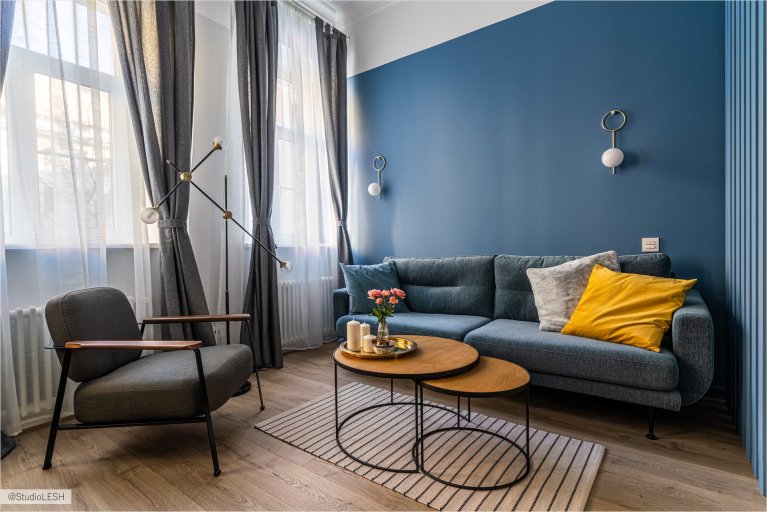 Современная гостиная с синими стенами, серым диваном, яркими подушками и стильными акцентами