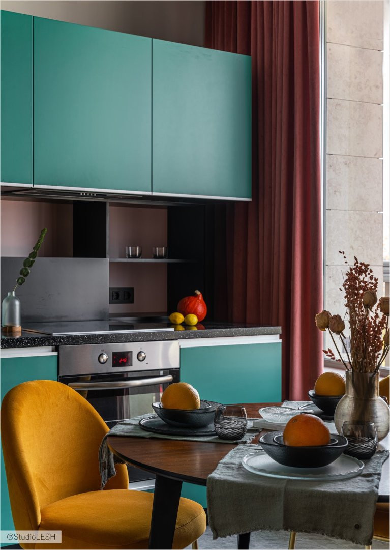 Дизайн кухни с бирюзовыми фасадами, темной столешницей, деревянным столом и желтым стулом
